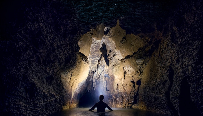 Person exploring illuminated cave during black water rafting in Waitomo.