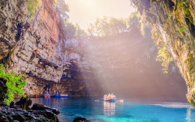 Boat tour inside Melissani Cave on Kefalonia Island, Greece, with sunlight illuminating the turquoise water.