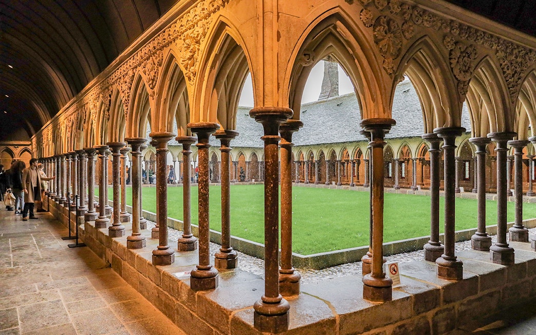 Cloister arches at Mont Saint Michel with visitors exploring the historic site.