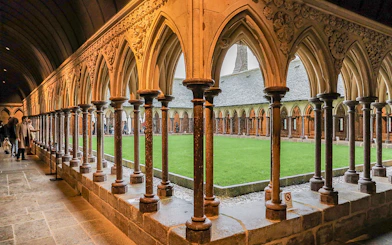 Cloister arches at Mont Saint Michel with visitors exploring the historic site.