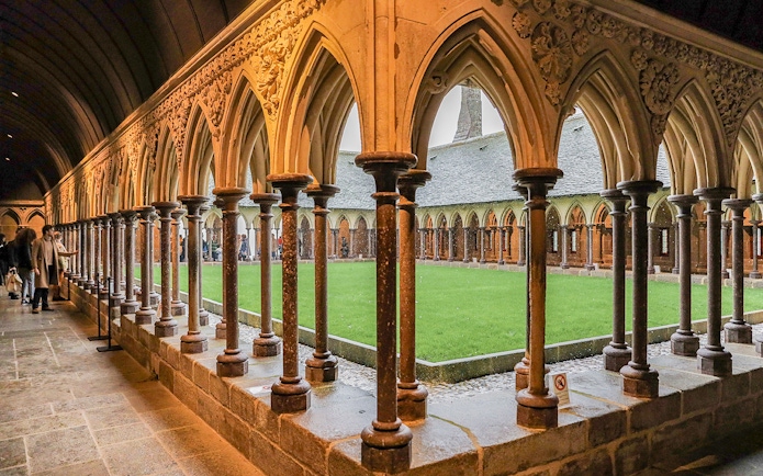 Cloister arches at Mont Saint Michel with visitors exploring the historic site.