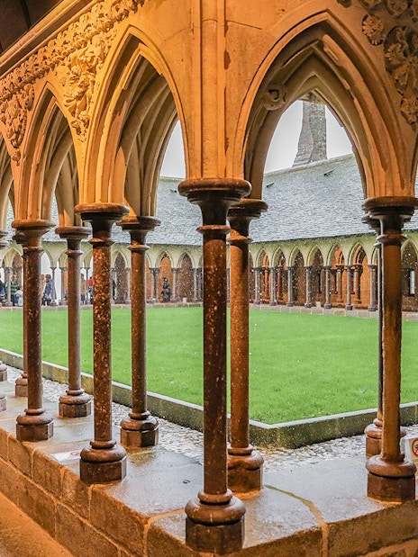Cloister arches at Mont Saint Michel with visitors exploring the historic site.