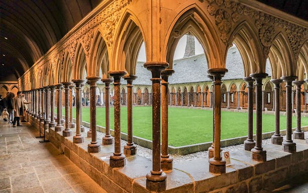 Cloister arches at Mont Saint Michel with visitors exploring the historic site.