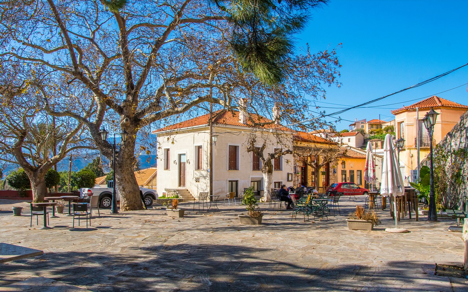 Central square in Chryso village, Delphi, Greece with trees and outdoor seating.