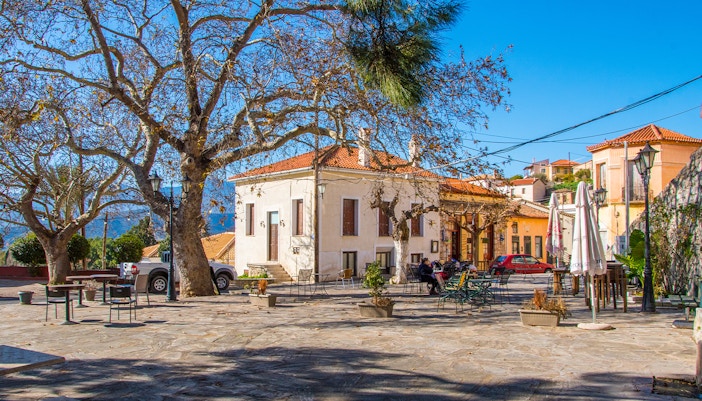 Central square in Chryso village, Delphi, Greece with trees and outdoor seating.