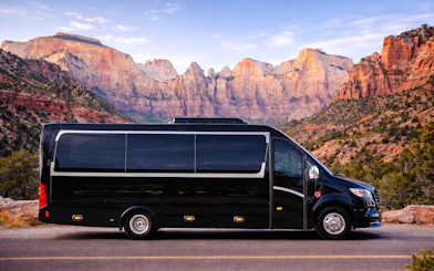 Luxury tour bus in front of Zion National Park's red rock cliffs.