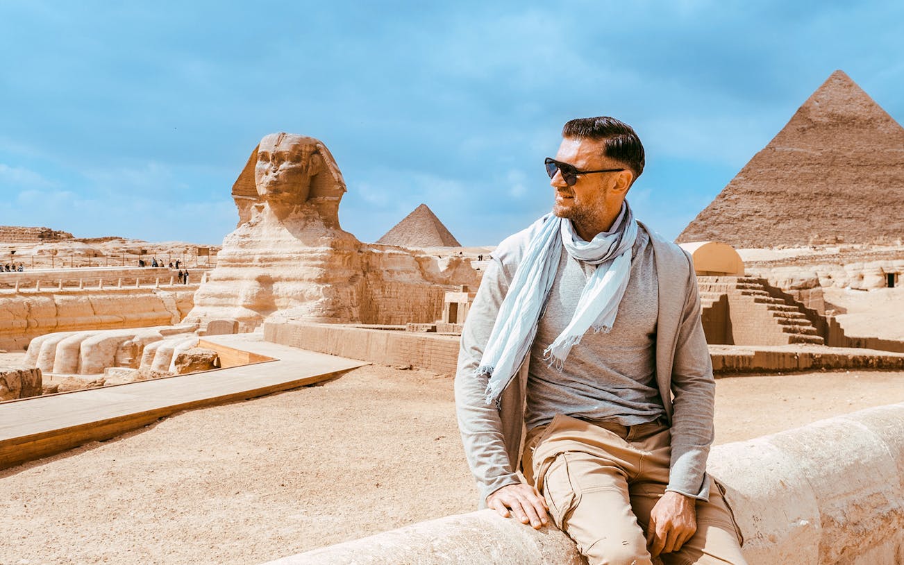 Tourist sitting near the Sphinx with Pyramid of Giza in the background.