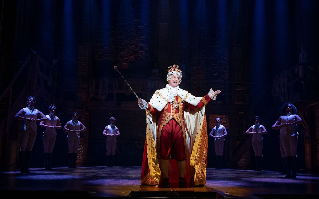 King character performing on stage in Hamilton musical.