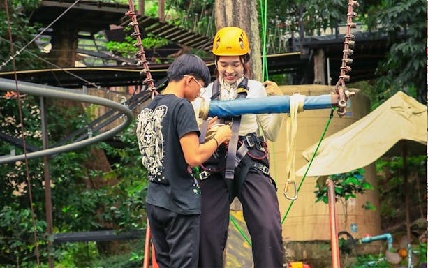 Staff member assists woman with zipline harness at Pongyang Adventure Park, Chiang Mai.