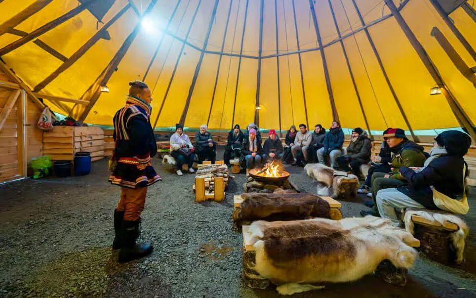 Sami guide speaking to tourists around a fire in a Tromsø lavvu tent.