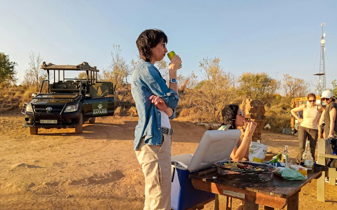Safari group enjoying refreshments at Pilanesberg Nature Reserve with safari vehicle in background.