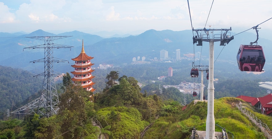 Cable cars ascending to Genting Highlands with a pagoda and lush hills in the background.