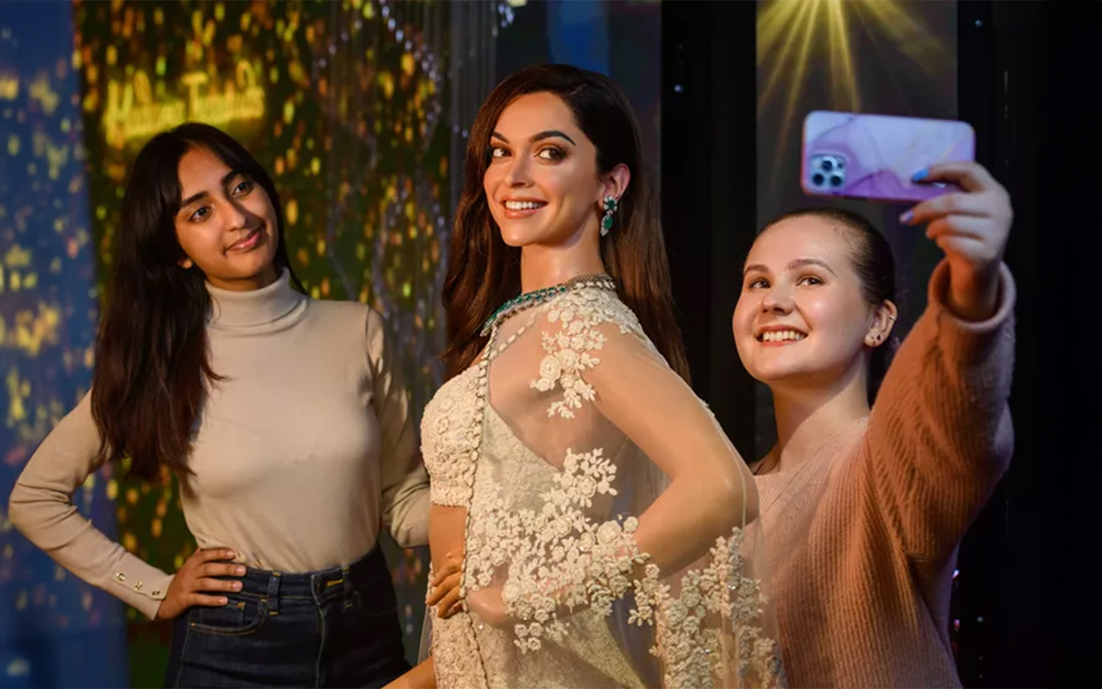 Two girls posing with wax figure of Deepika Padukone, dresses in an Indian traditional attire called Lehenga