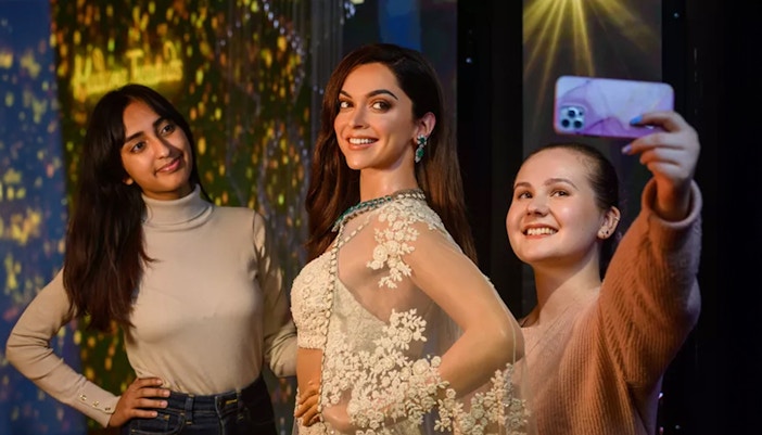 Two girls posing with wax figure of Deepika Padukone, dresses in an Indian traditional attire called Lehenga