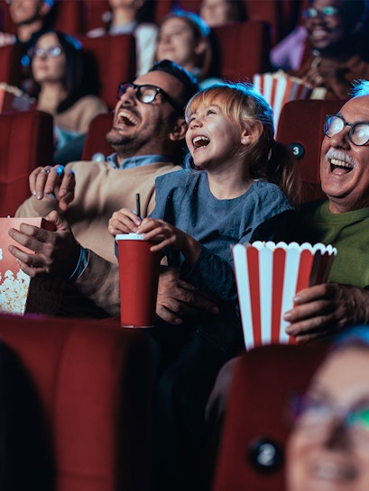 Audience enjoying a movie in a theater with popcorn and drinks.