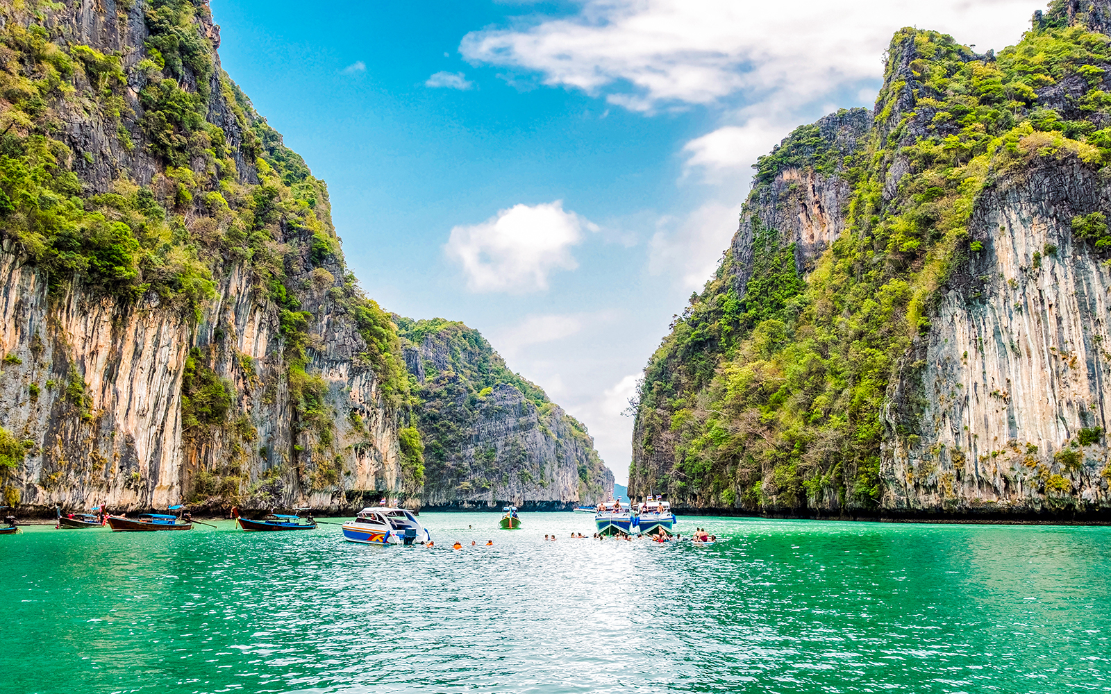Boats and swimmers in Pileh Lagoon, surrounded by limestone cliffs, Krabi, Thailand.