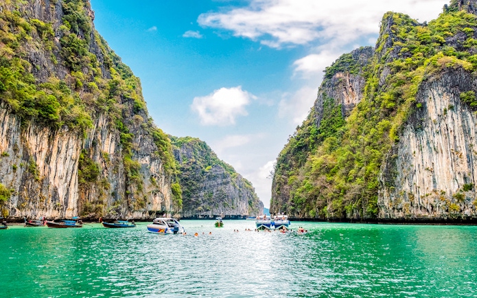 Boats and swimmers in Pileh Lagoon, surrounded by limestone cliffs, Krabi, Thailand.