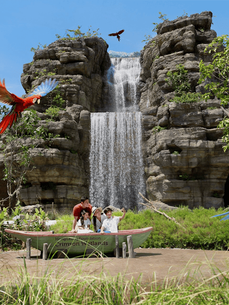 Family enjoying a boat ride at Hong Leong Foundation Crimson Wetlands with waterfall and colorful parrots.