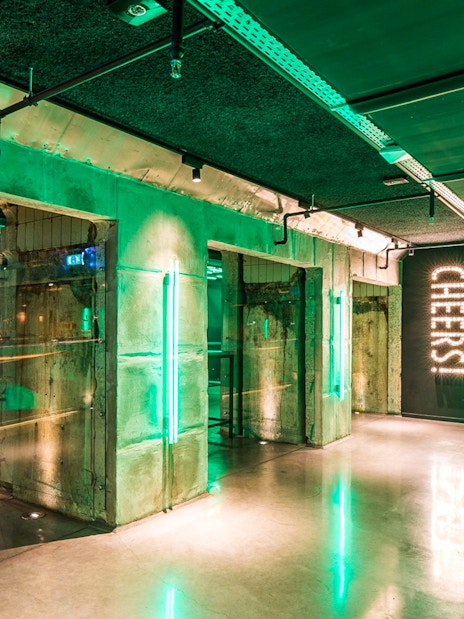 Heineken Experience bar area with green lighting and "Cheers" sign in Amsterdam.