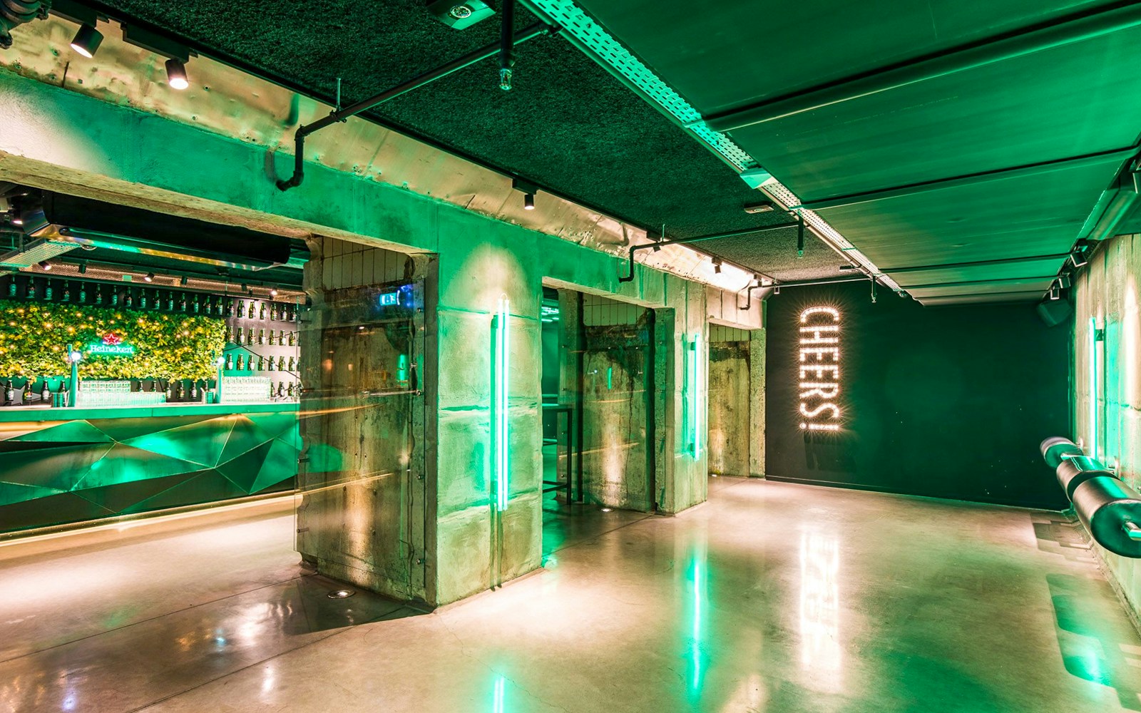 Heineken Experience bar area with green lighting and "Cheers" sign in Amsterdam.