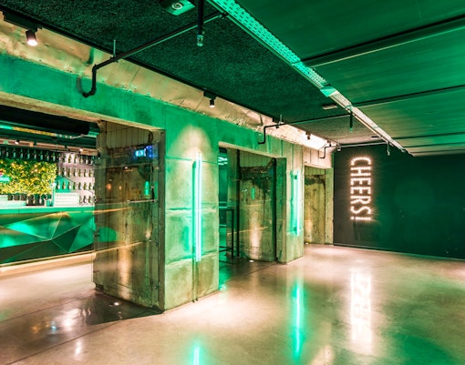 Heineken Experience bar area with green lighting and "Cheers" sign in Amsterdam.