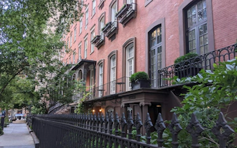Historic brownstone buildings along a tree-lined street in New York City.