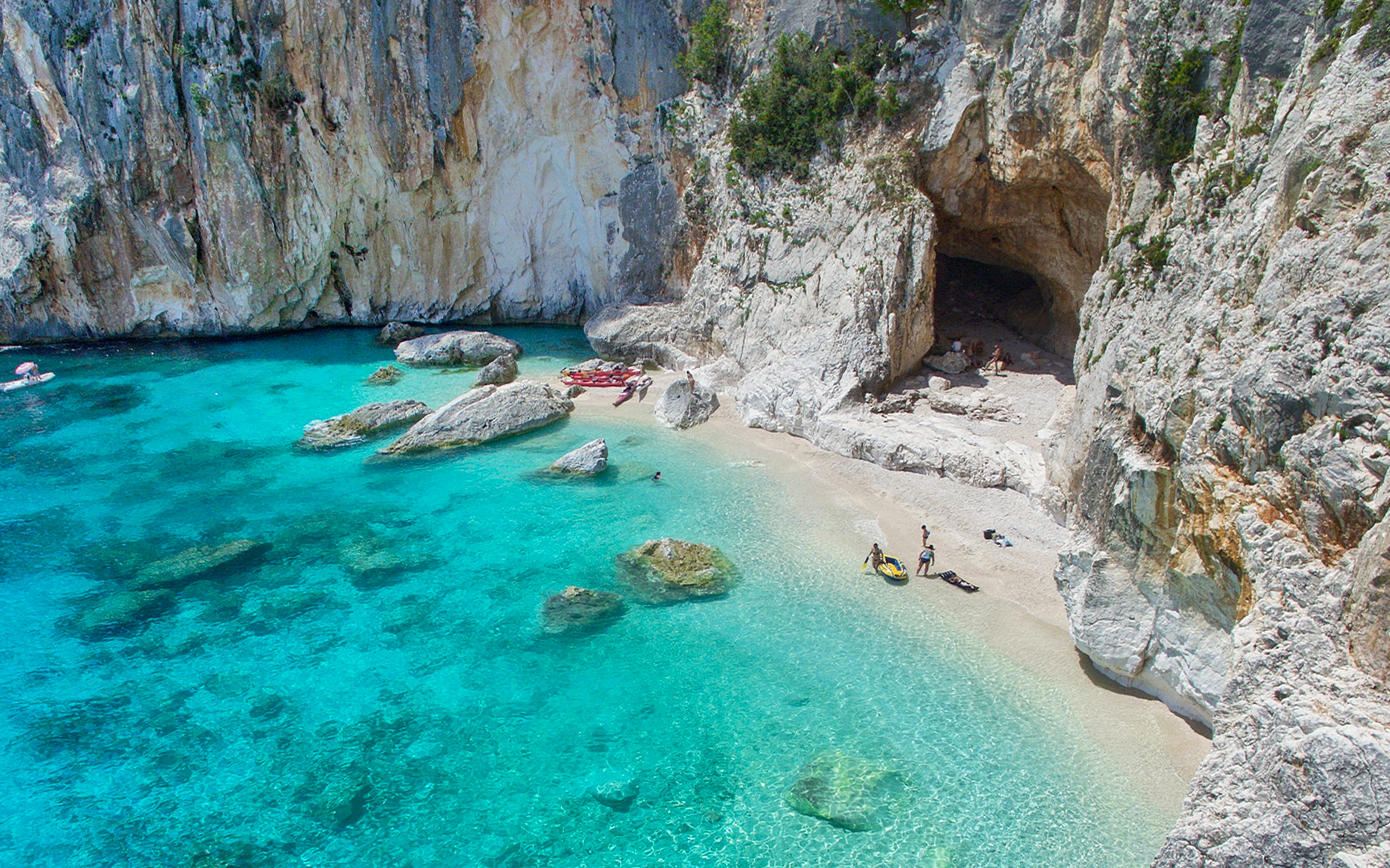 Cave entrance by turquoise waters on a Sardinian beach with rocky cliffs.