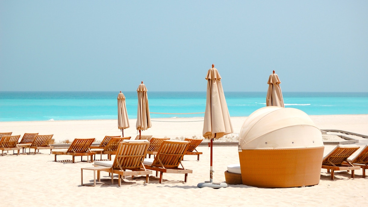 Beach chairs and umbrellas on Saadiyat Island, Abu Dhabi, overlooking turquoise sea.