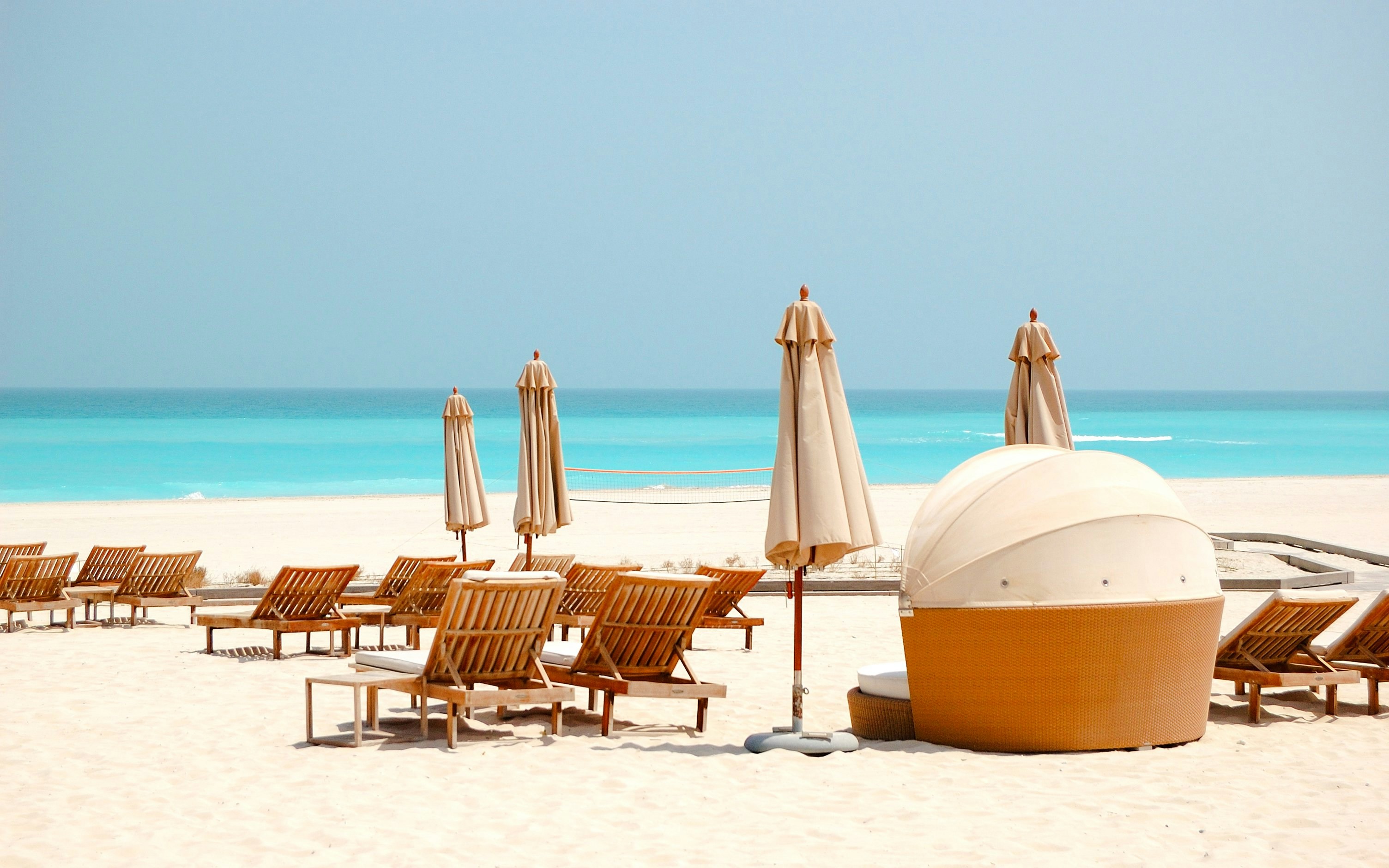 Beach chairs and umbrellas on Saadiyat Island, Abu Dhabi, overlooking turquoise sea.