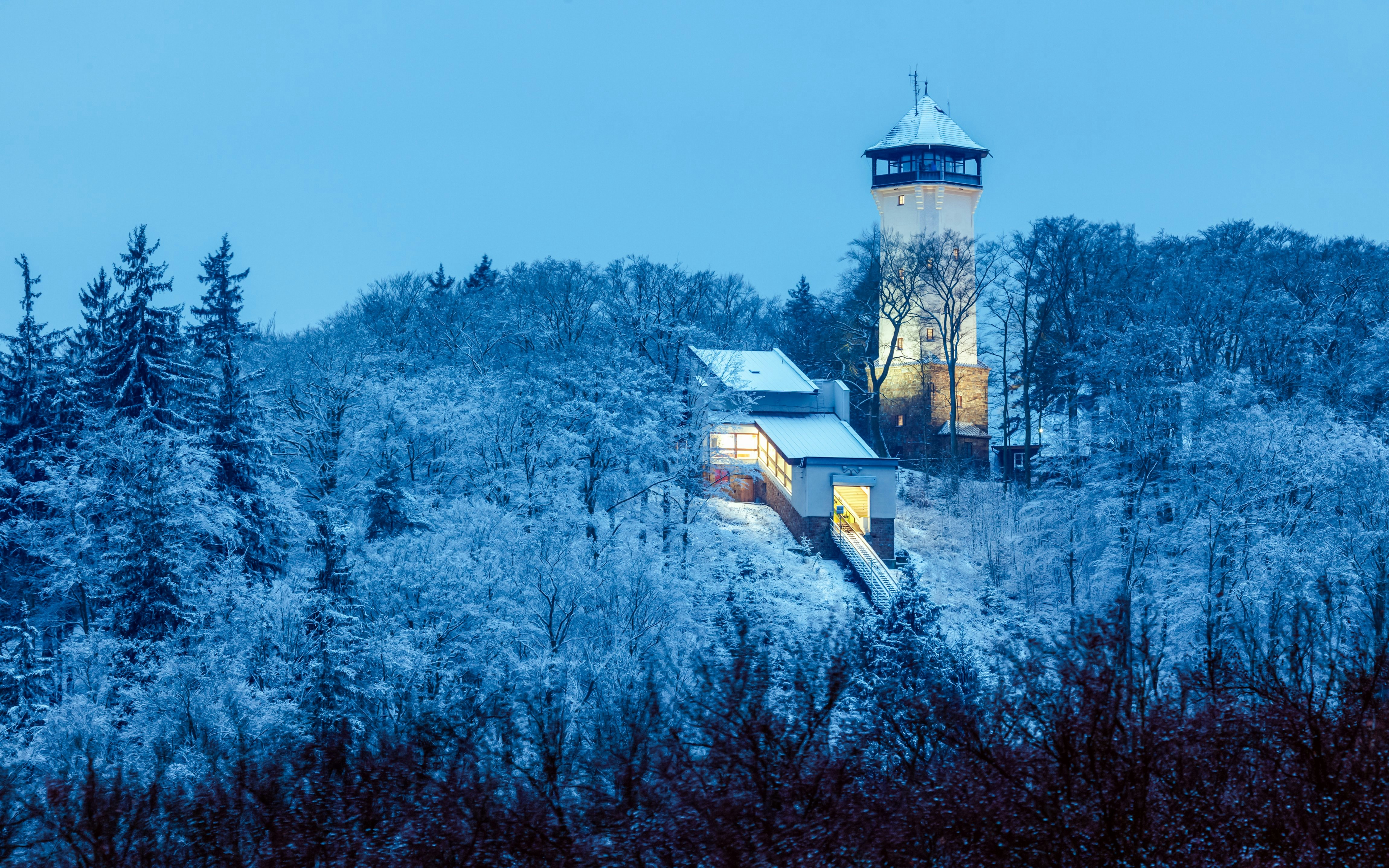 Diana Tower in Karlovy Vary surrounded by snow-covered trees at dusk.