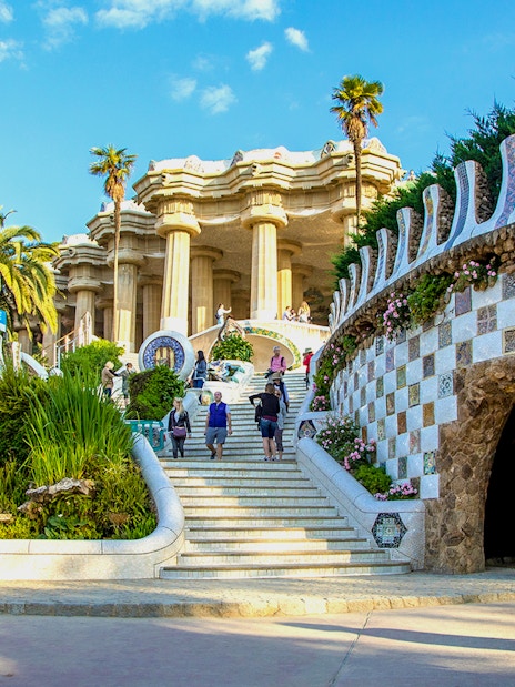 Park Güell entrance with mosaic walls and visitors in Barcelona, Spain.