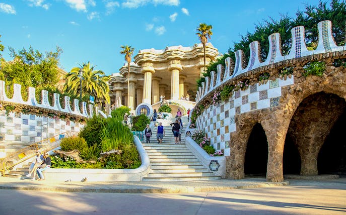Park Güell entrance with mosaic walls and visitors in Barcelona, Spain.