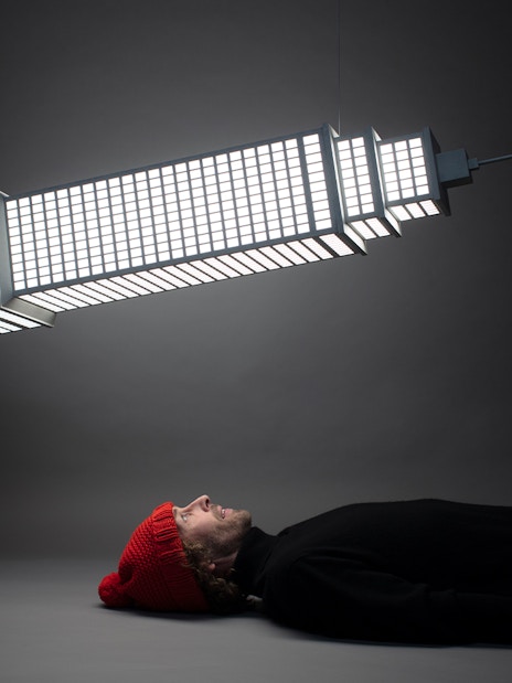 Man lying beneath illuminated sculpture at Amsterdam Moco Museum's Planet Positive Disruption exhibit by Frankey.