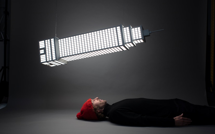 Man lying beneath illuminated sculpture at Amsterdam Moco Museum's Planet Positive Disruption exhibit by Frankey.
