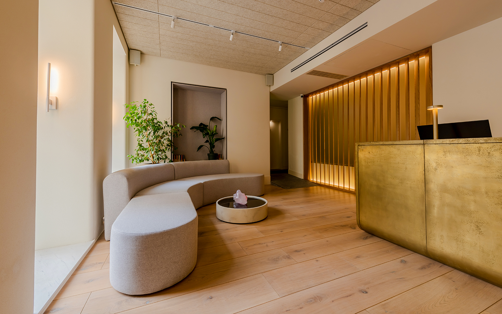 Modern luxury hotel reception with curved seating, plants, and a gold-toned front desk.