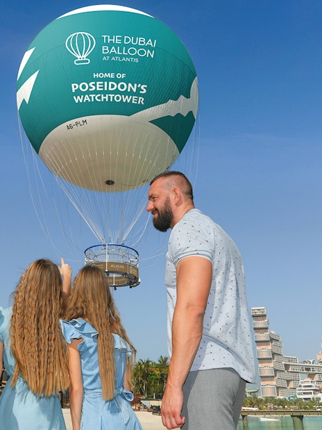 Family observing The Dubai Balloon at Atlantis with resort in background.