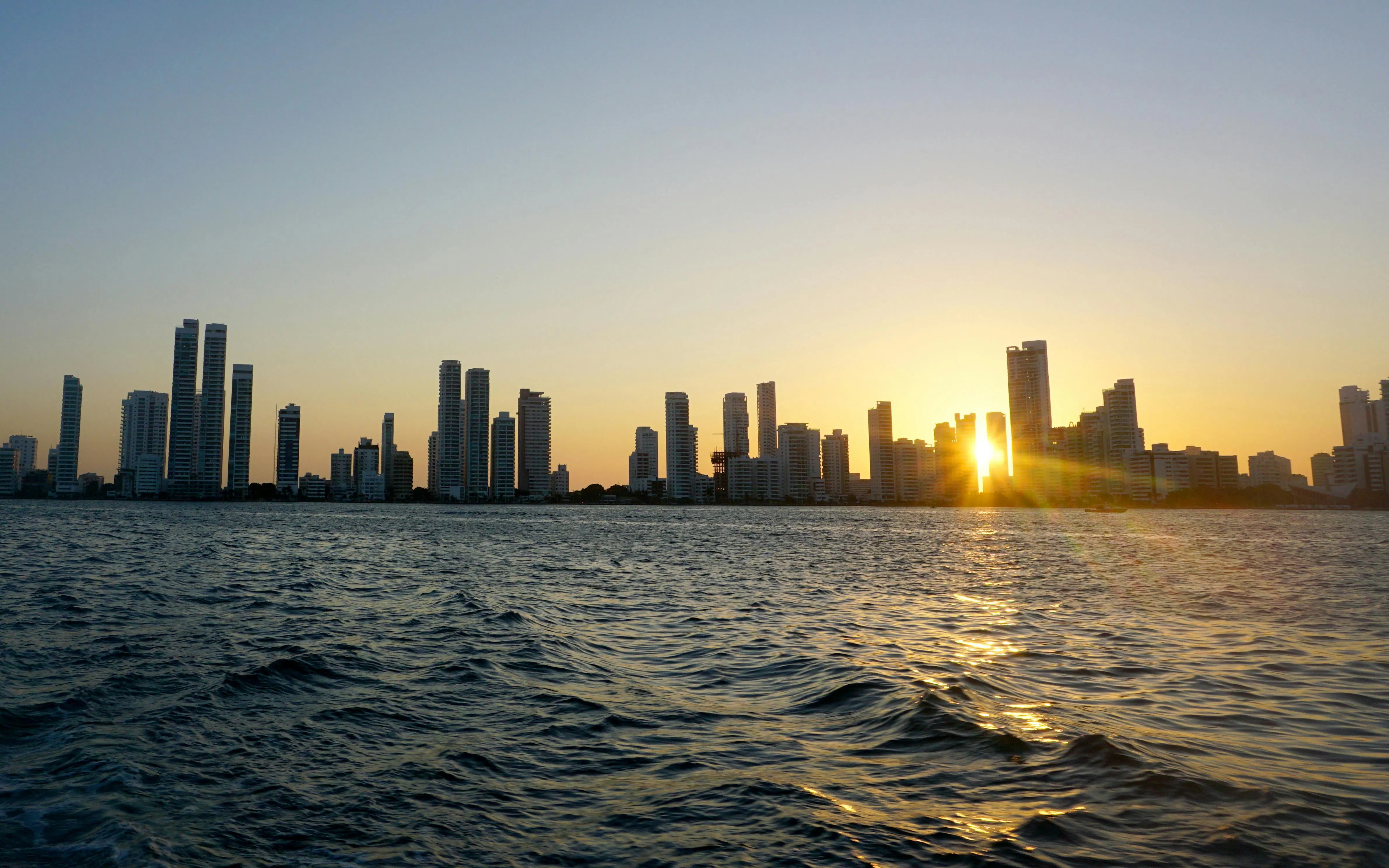 Cartagena skyline at sunset with sun setting behind high-rise buildings.