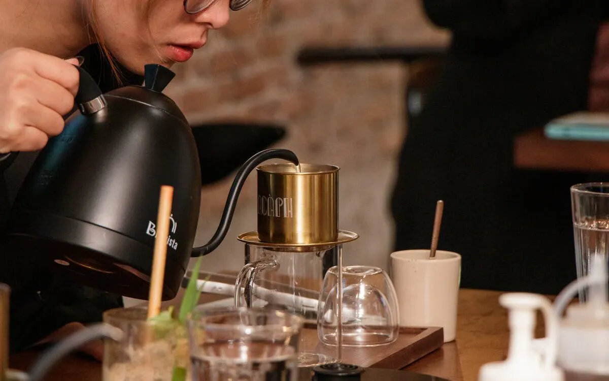 Pouring hot water into a Vietnamese coffee filter during a cultural tour.