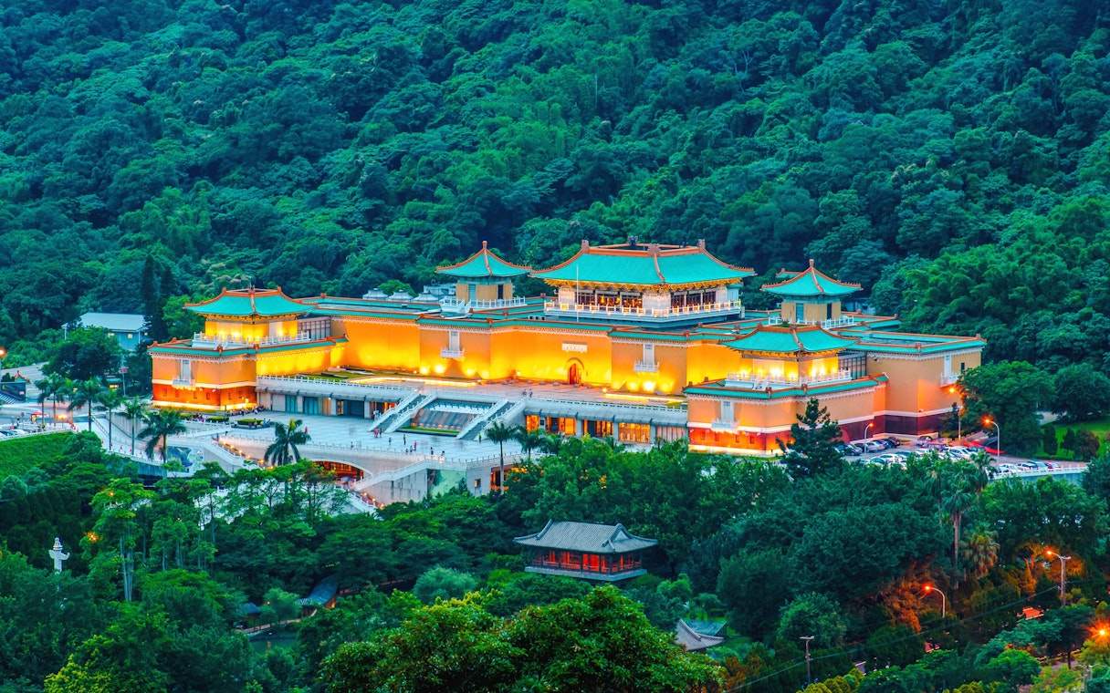 National Palace Museum Taipei illuminated at dusk, surrounded by lush greenery.