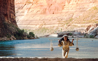 Person carrying a stick with baskets by the Colorado River in the Grand Canyon.