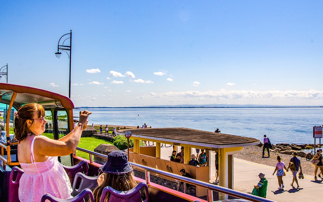 Lady photographing scenic view from Hop-On Hop-Off bus in Galway, Ireland.