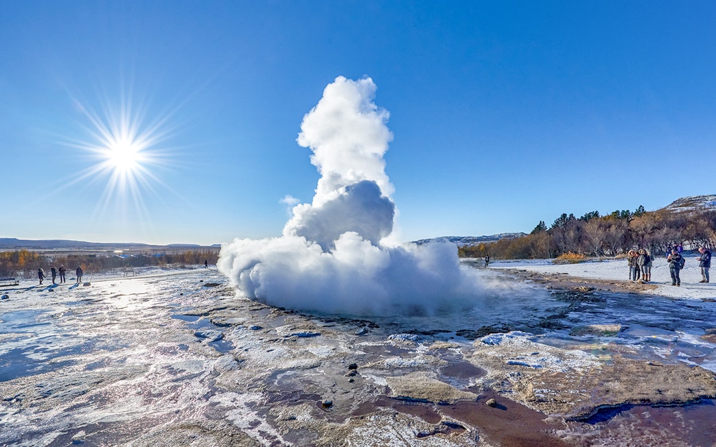 Strokkur Geyser erupting with steam in Iceland's geothermal area under a clear blue sky.