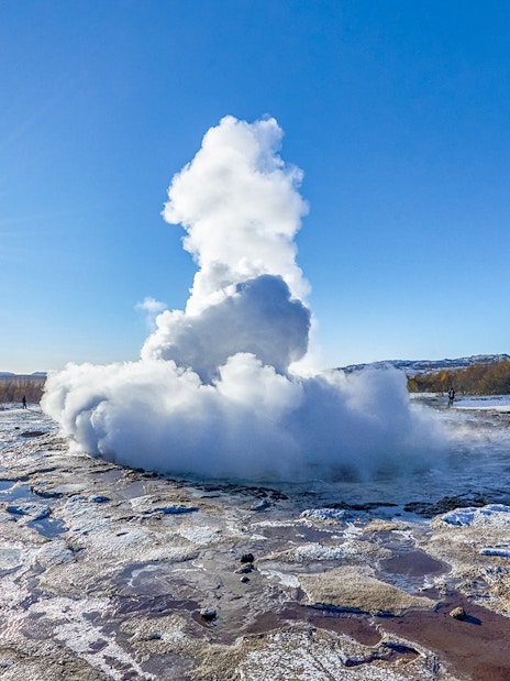 Strokkur Geyser erupting with steam in Iceland's geothermal area under a clear blue sky.