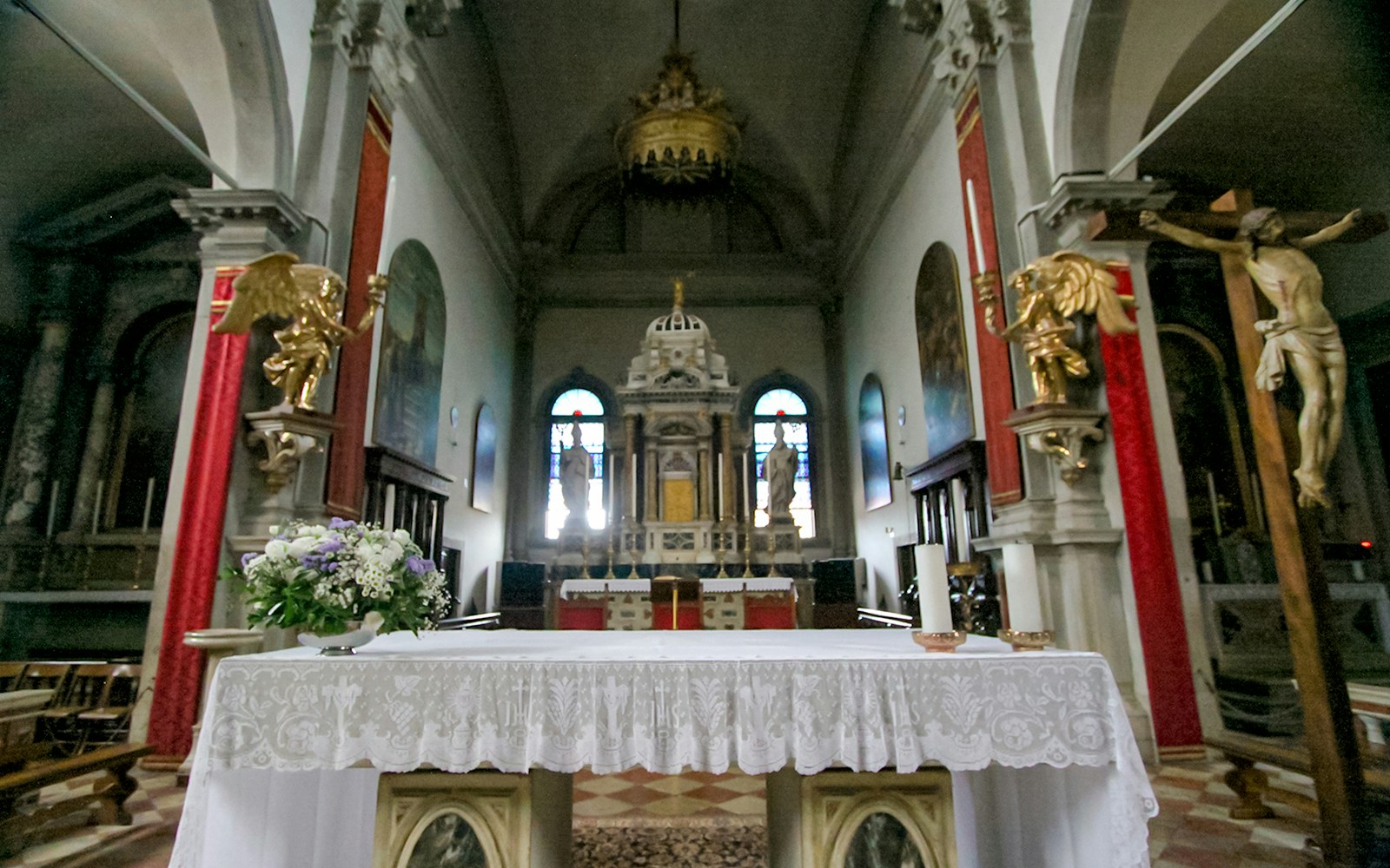 Altar with lace cloth in Burano church interior, featuring ornate decorations and statues.