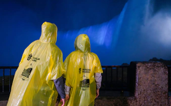 Visitors in yellow ponchos view Niagara Falls illuminated at night.