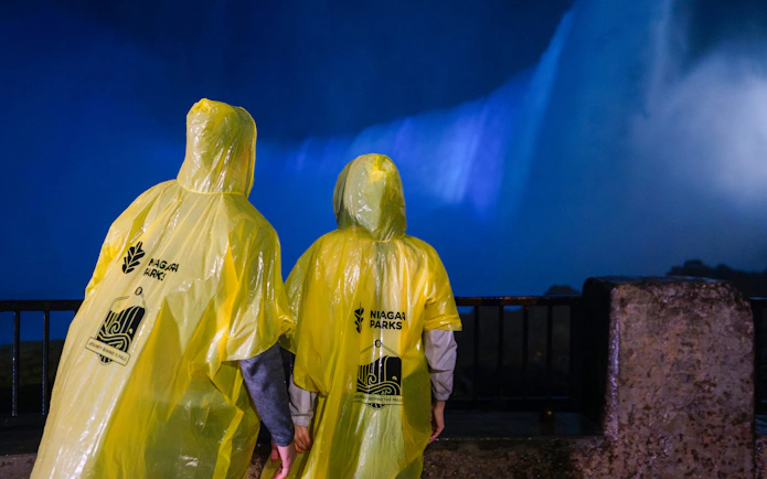 Visitors in yellow ponchos view Niagara Falls illuminated at night.