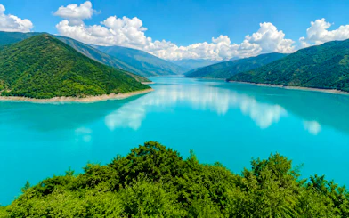 Zhinvali Water Reservoir in Georgia with surrounding green hills and clear blue sky.