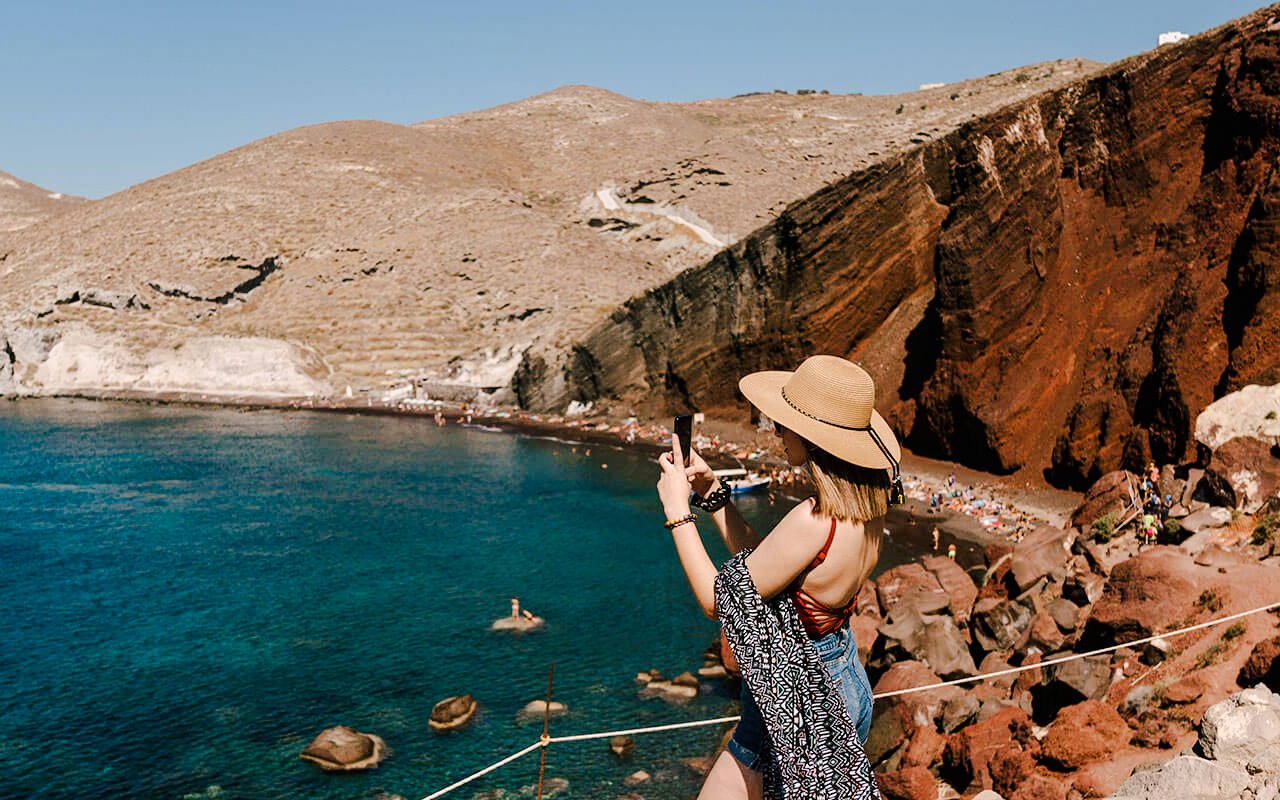 Woman photographing Red Beach cliffs in Santorini, Greece.