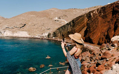 Woman photographing Red Beach cliffs in Santorini, Greece.