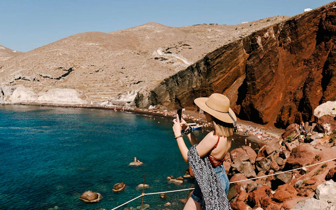 Woman photographing Red Beach cliffs in Santorini, Greece.